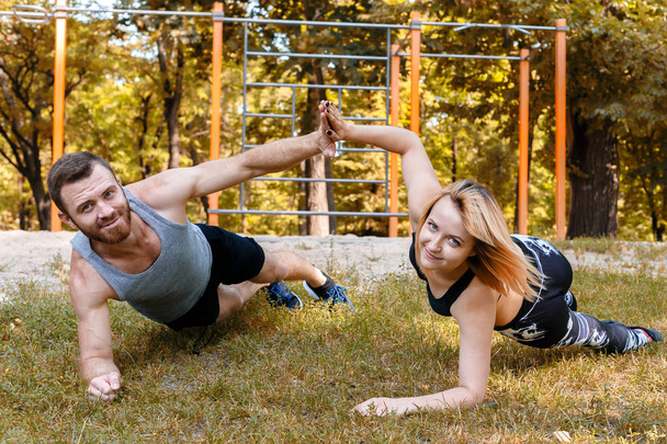 Young blond girl and bearded man doing exercise plank at sunny a - 写真・画像