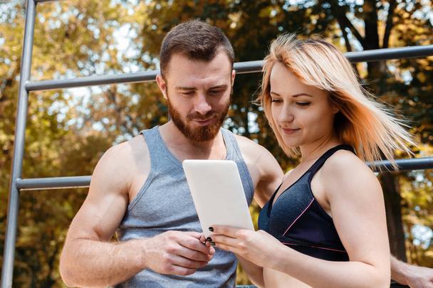 Young athletic girl and bearded man browsing the internet on tab - Photo, image