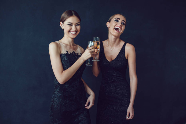 Houkuttelevat naiset cocktail-mekoissa pitävät samppanjaa, puhuvat ja hymyilevät.
. - Valokuva, kuva