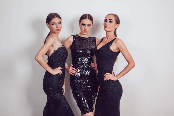 Attractive girls in black cocktail dresses on a grey background. - Foto, Imagen
