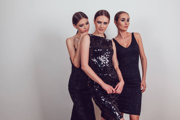 Attractive girls in black cocktail dresses on a grey background. - Фото, изображение