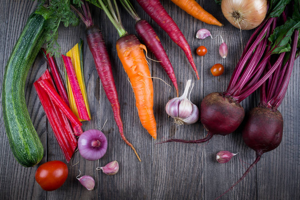 Top view of fresh vegetables, spices on rustic dark background. Carrot, beet, chard, zucchini, onion, garlic, tomato. Harvest/gardening concept. - Fotografie, Obrázek