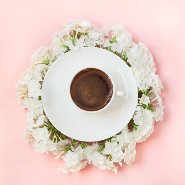 Creative flat lay, morning black coffee and white flower phlox around on pink. View from above. - Фото, изображение