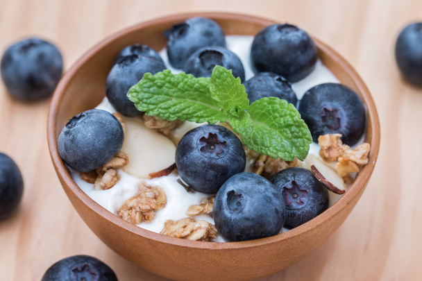Yogurt with granola and organic blueberries in wooden bowl. - Фото, зображення