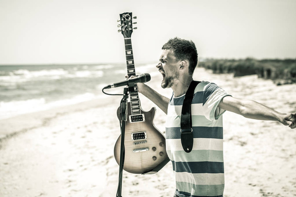 岩ビーチ、ミュージシャンがギターを弾き、レジャーと創造性の概念、マイクに向かって歌う - 写真・画像