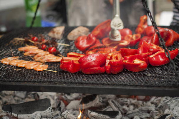 Pimienta roja, tomates y camarones en brochetas se cocinan en una parrilla
 - Foto, imagen
