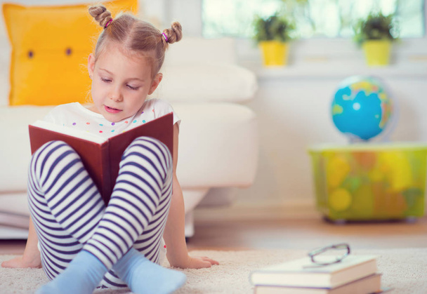 Portrait of clever little girl sitting with book on the floor  - Foto, Bild