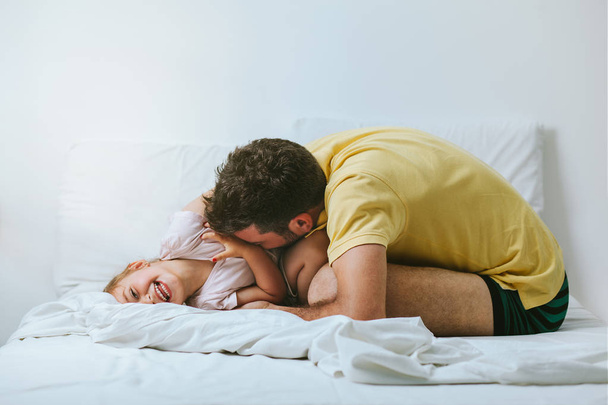 Vader en dochter spelen en lachen in bed - Foto, afbeelding