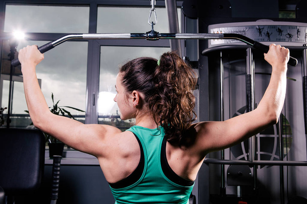 Задний вид тренированной девушки, делающей упражнения. Тренировка мышц спины
 - Фото, изображение
