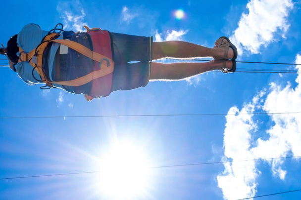 Ucrania, Migea - 30 de junio de 2017: Zipline. Una vista de un hombre deslizándose sobre un cable de acero contra un hermoso cielo azul con nubes blancas. Descanso extremo y activo
. - Foto, imagen