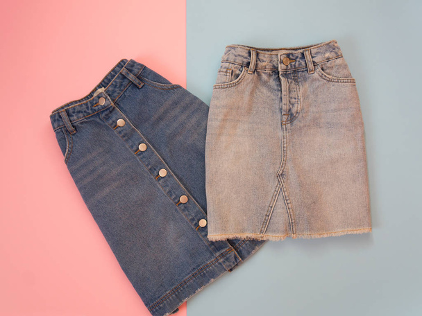Модная концепция. Две джинсовые юбки, голубая и серая. Нежный розовый и синий фон
. - Фото, изображение