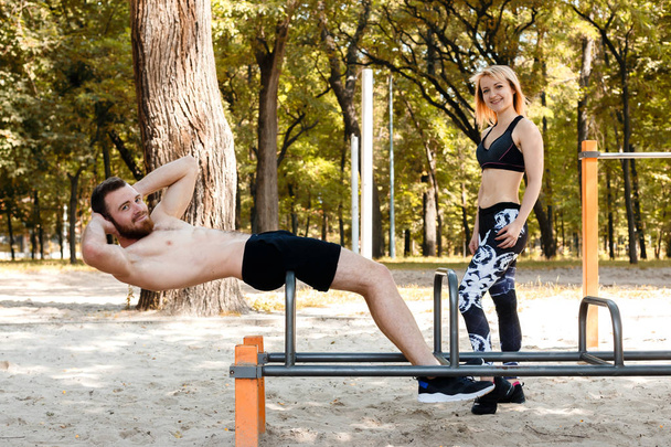 Sporty young couple pumping abdominal muscles in a park at autum - Valokuva, kuva