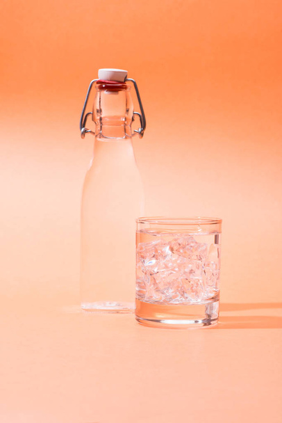 Drinking water in a bottle and glass of ice over orange backgrou - Photo, Image