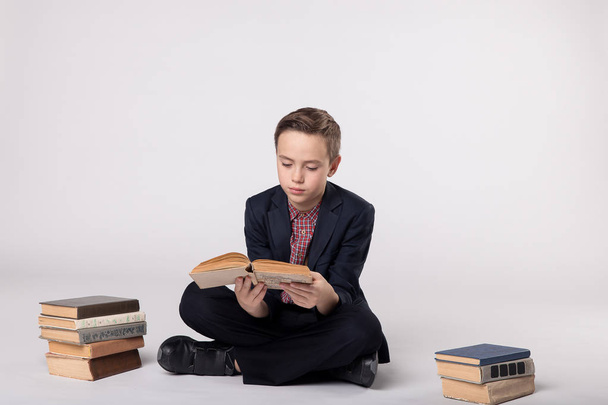Χαριτωμένο αγόρι σε ένα κοστούμι που κάθεται και κρατά ένα βιβλίο σε λευκό φόντο - Φωτογραφία, εικόνα