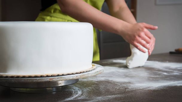 Unrecognisable woman preparing white fondant for cake decorating, hands detail, focus on the cake - Фото, изображение