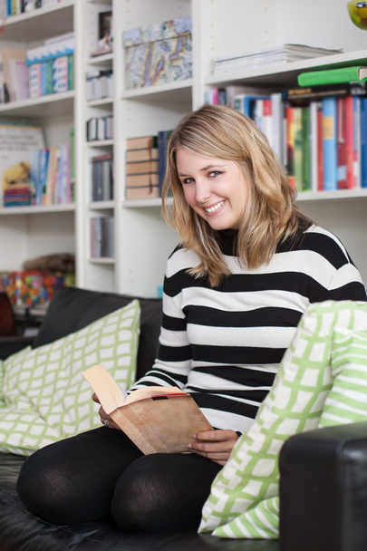 Young, attractive woman sits on the couch and reads a book - Foto, imagen