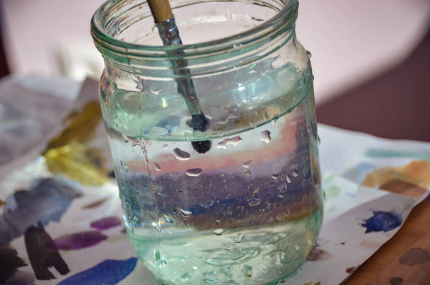 Paintbrush in clean water between bright paints in artist studio  - Photo, image