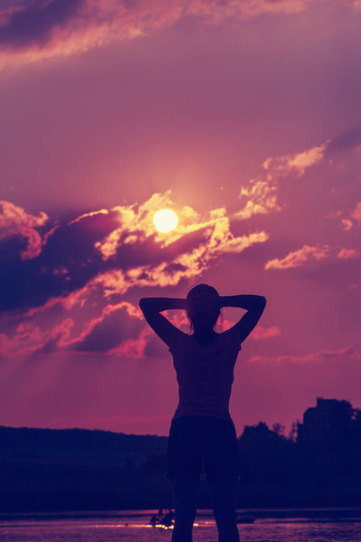 Silhueta de uma jovem mulher com os braços levantados no fundo do pôr-do-sol
 - Foto, Imagem