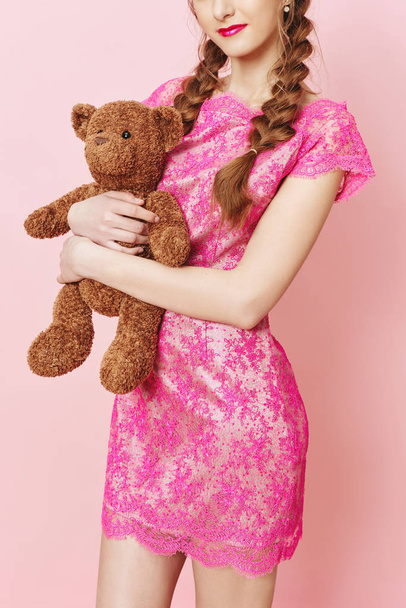 Fashion photo of young girl posing with Teddy bear over pink background in studio - Фото, изображение