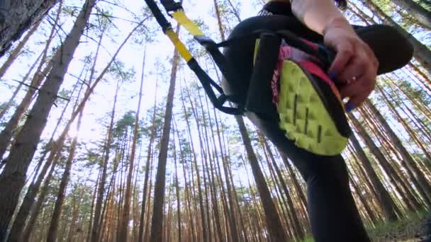 athletic, woman, coach, instructor, performs, doing exercises with fitness trx system, TRX suspension straps. In pine forest, in summer, in sun rays. View from below, view of the feet - Séquence, vidéo