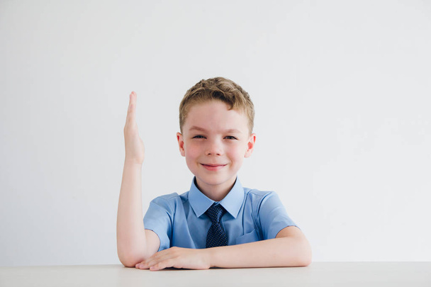 Schoolboy in school uniform raises his hand at the Desk - Fotoğraf, Görsel
