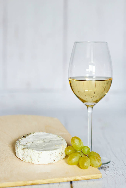 Sklo bílé víno, sýr camembert a bílých hroznů na dřevěné pozadí - Fotografie, Obrázek