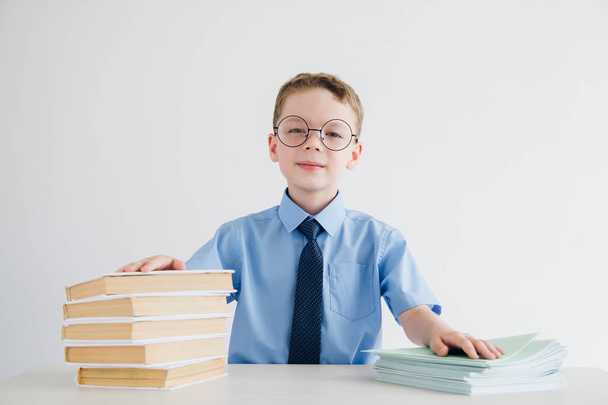 Schoolboy in school uniform sitting at a Desk with textbooks and - Fotografie, Obrázek