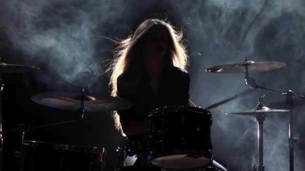 Girl is kicks from playing drums, playing energetic music. Black smoke background. Silhouette. Slow motion - Filmagem, Vídeo
