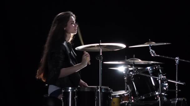 Girl drummer with chopsticks beats rhythmic music. Black background. Side view. Slow motion - Felvétel, videó