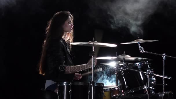 Girl plays the drum she likes to pound on pancakes. Black smoke background. Side view. Slow motion - Metraje, vídeo