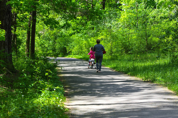 Dabuschka und Enkelin fahren Fahrrad im Stadtpark. Mai  - Foto, Bild