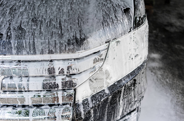 Πλύσιμο αυτοκινήτων με σαπούνι. Μαύρο αυτοκίνητο καλύπτονται από αφρώδες υλικό. - Φωτογραφία, εικόνα