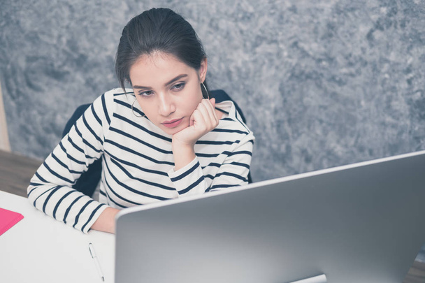 Hermosa mujer joven mirando una pantalla de ordenador y pensando en la oficina, estresada y nerviosa - Foto, imagen