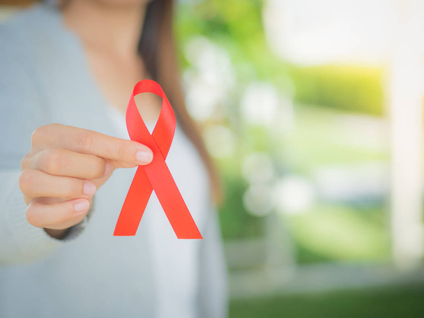 Closeup woman hand holding red ribbon HIV, world AIDS day awareness ribbon.  Healthcare and medicine concept. - Foto, Imagem