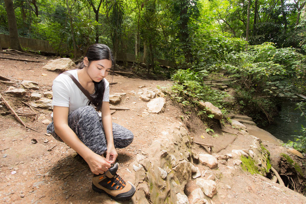Азиатка завязывает шнурки в лесу.
 - Фото, изображение