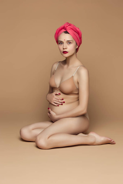 Young beautiful pregnant woman sitting on brown background - Фото, зображення