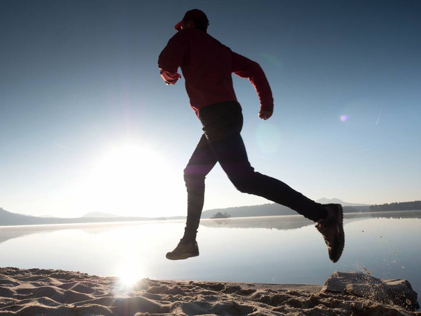 Hombre alto en forma corriendo rápido por el mar en la playa. Potente entrenamiento de corredor al aire libre en la mañana de verano
. - Foto, Imagen