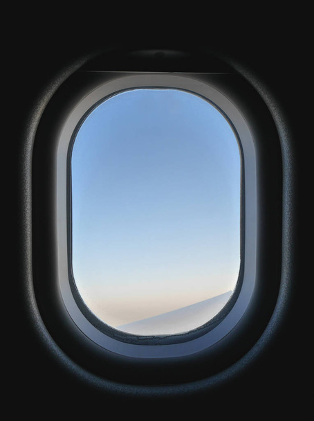 Вид на замерзле вікно літака зсередини, бачимо блакитне і рожеве небо і частину крила літака. Всередині літака темно, але зовні яскравий час доби.
. - Фото, зображення