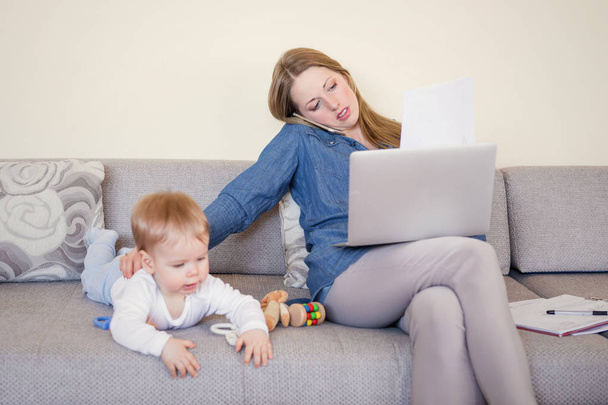 Werkende moeder met baby op de Bank, die op laptop werkt en praten over de telefoon - Foto, afbeelding
