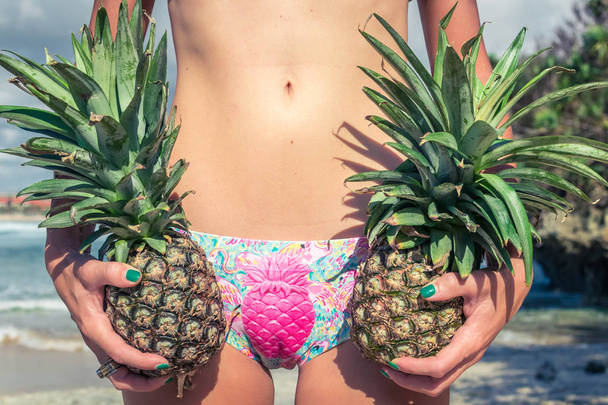 Giovane donna tropicale sexy corpo da vicino con ananas. Donna del corpo fitness sulla spiaggia. Isola di Bali
. - Foto, immagini
