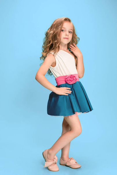 Full length of beautiful little girl in dress standing and posing over blue background - Foto, afbeelding