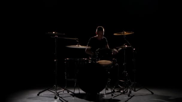 Professional musician plays music on drums with the help of sticks. Black background. Silhouette - Video, Çekim