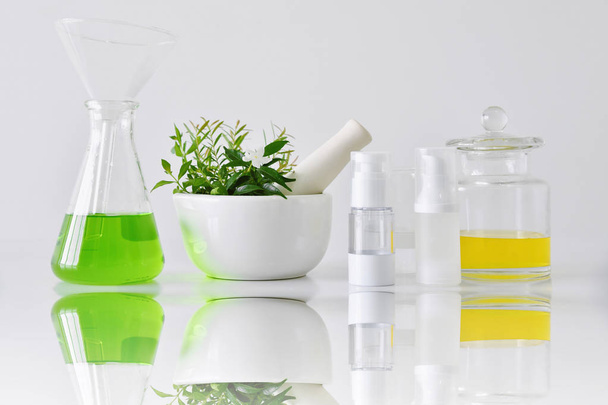 緑ハーブの葉と実験用ガラス器具、化粧品ボトル容器モックアップをブランディングのための空白のラベルのパッケージに焦点を当てる - 写真・画像