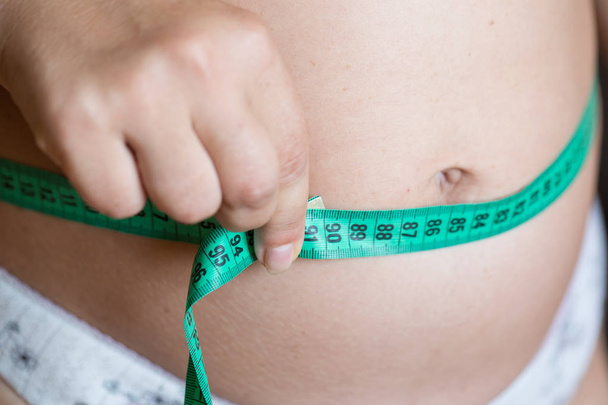 Vrouwen meten haar maag met een meetlint - Foto, afbeelding