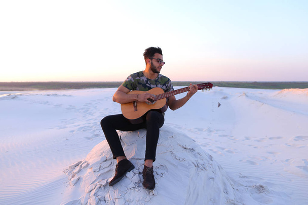 Cute young male Arab enjoys sound of guitar, sitting on hill in - Photo, Image