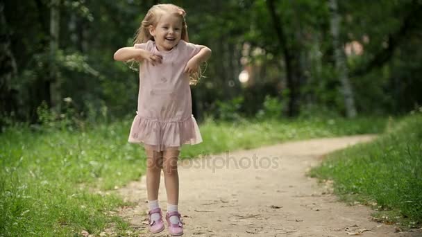 Aranyos szőke gyermek lány forog a parkban, lassú mozgás - Felvétel, videó