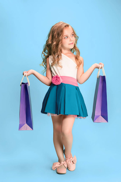 The cute little caucasian brunette girl in dress holding shopping bags - Фото, изображение