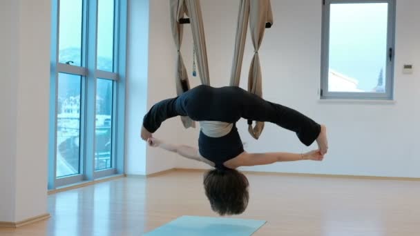 Young woman swings upside down in hammock studio indoors. - Footage, Video