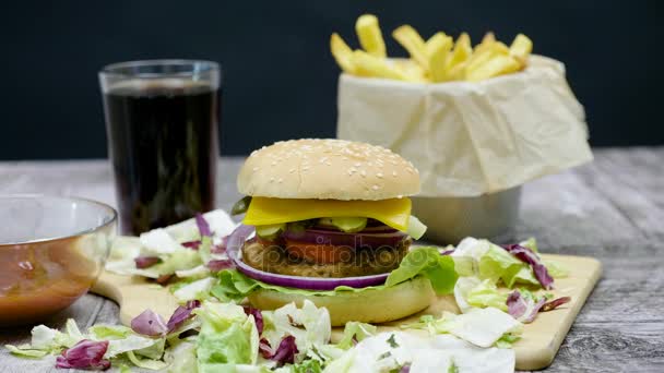 Schuss Burger, Pommes, Cola und Ketchup auf Holztisch vor schwarzem Hintergrund - Filmmaterial, Video