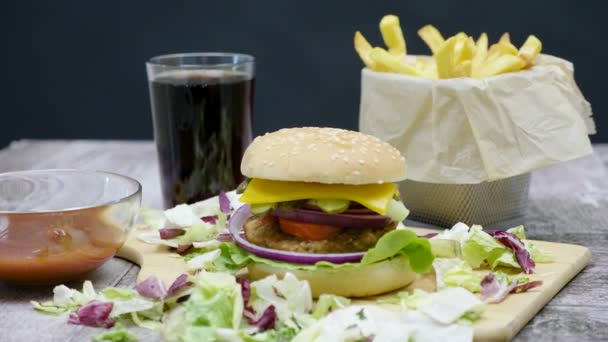 Burger, πατάτες τηγανητές, αναψυκτικά τύπου κόλα και κέτσαπ στο ξύλινο τραπέζι πάνω από το μαύρο φόντο - Πλάνα, βίντεο
